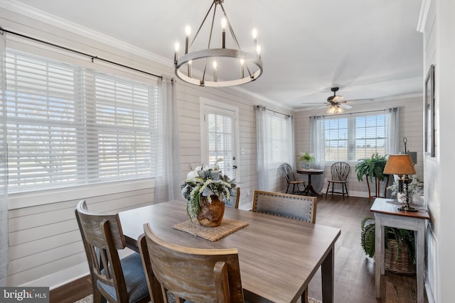 dining area with wooden walls, ceiling fan with notable chandelier, crown molding, and wood finished floors