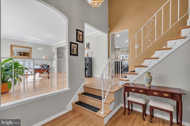 stairs with arched walkways, wood finished floors, and baseboards