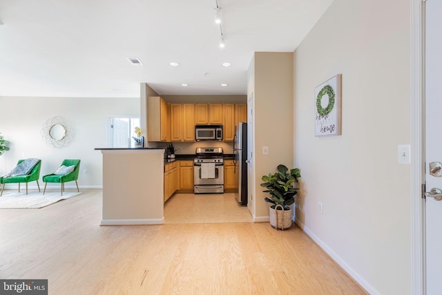 kitchen featuring rail lighting, appliances with stainless steel finishes, light wood-type flooring, and kitchen peninsula