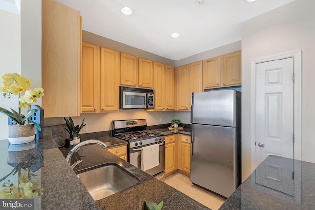 kitchen with appliances with stainless steel finishes, sink, light brown cabinets, and dark stone countertops