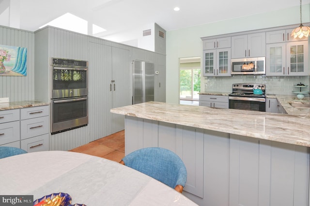 kitchen featuring glass insert cabinets, pendant lighting, stainless steel appliances, and light stone counters