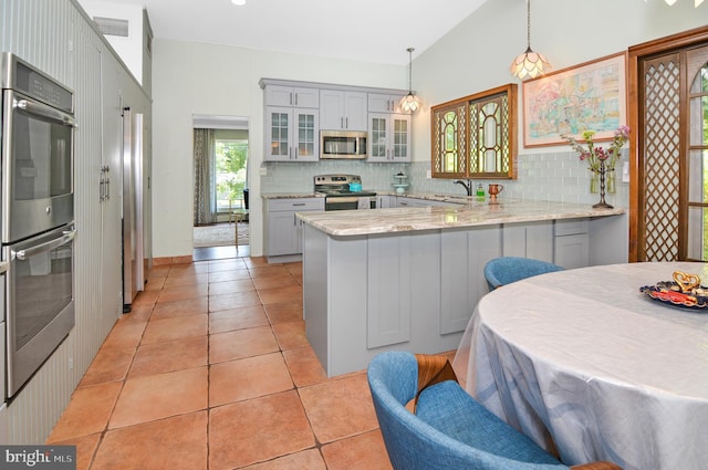 kitchen featuring stainless steel appliances, a peninsula, gray cabinets, glass insert cabinets, and pendant lighting