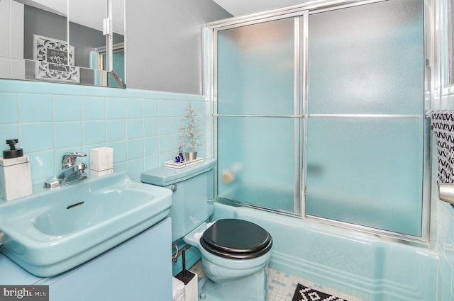 bathroom featuring tile patterned flooring, toilet, bath / shower combo with glass door, vanity, and tile walls