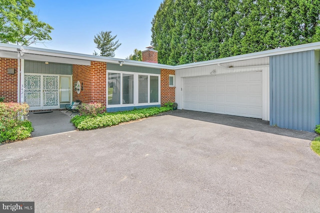 view of front facade featuring aphalt driveway, brick siding, a chimney, and an attached garage