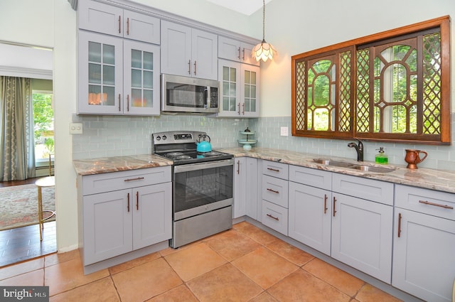 kitchen featuring decorative light fixtures, stainless steel appliances, backsplash, a sink, and light stone countertops