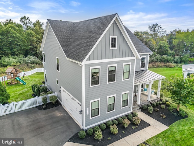 view of front facade with a playground, a garage, a front lawn, and covered porch