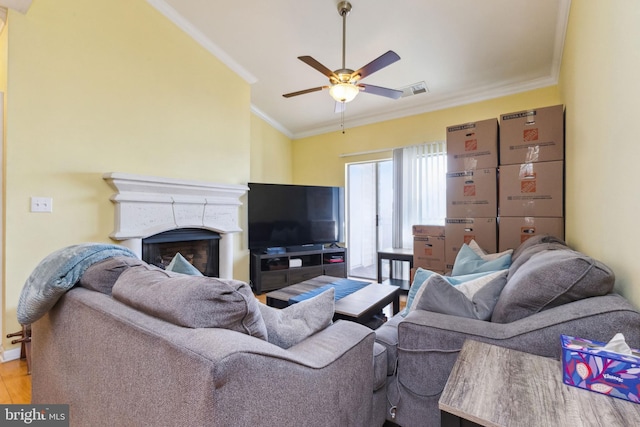 living room featuring ceiling fan, a fireplace, ornamental molding, and wood finished floors