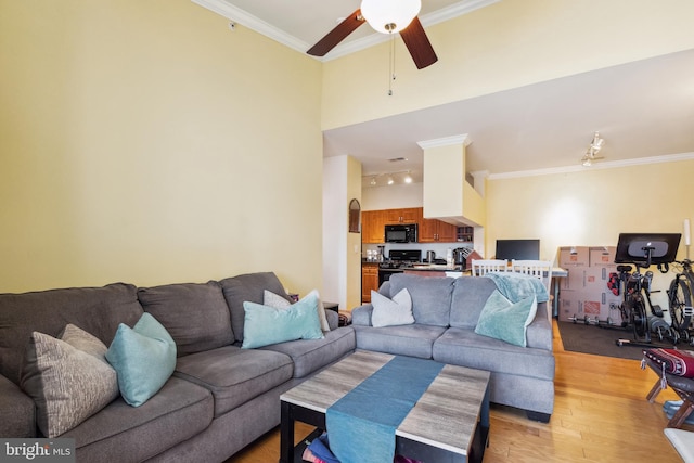 living room featuring a towering ceiling, light wood finished floors, ceiling fan, and ornamental molding