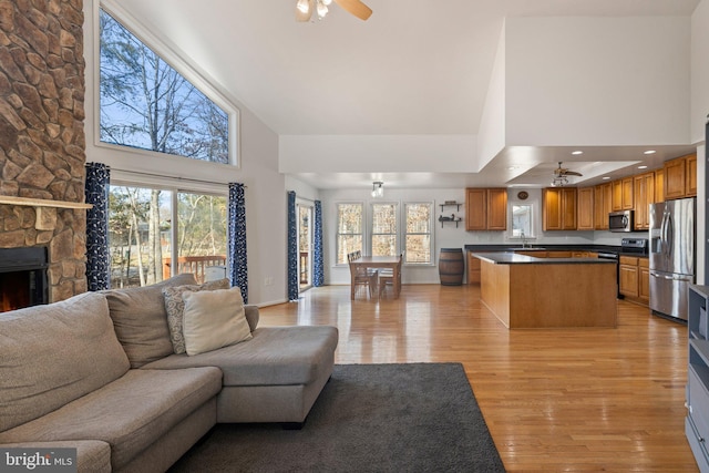 living room featuring a stone fireplace, light wood-style flooring, plenty of natural light, and a ceiling fan