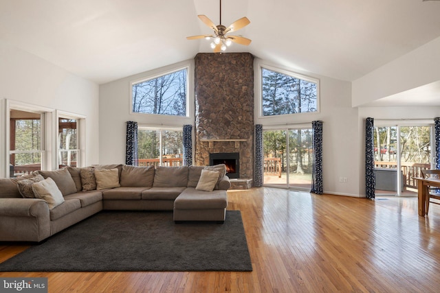 living area with high vaulted ceiling, a stone fireplace, hardwood / wood-style floors, and a ceiling fan