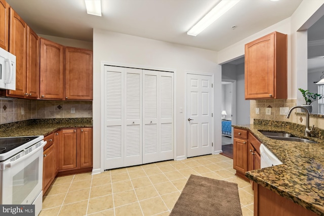 kitchen featuring light tile patterned flooring, sink, dark stone countertops, white appliances, and decorative backsplash