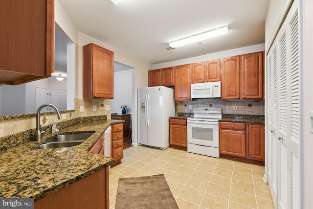 kitchen featuring light tile patterned flooring, sink, dark stone countertops, and white appliances