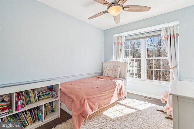 bedroom with a ceiling fan, visible vents, baseboards, and wood finished floors