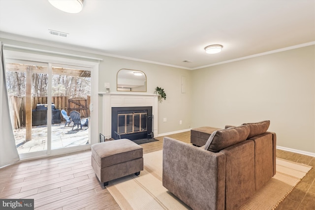 living room featuring baseboards, a fireplace with flush hearth, ornamental molding, and wood finished floors