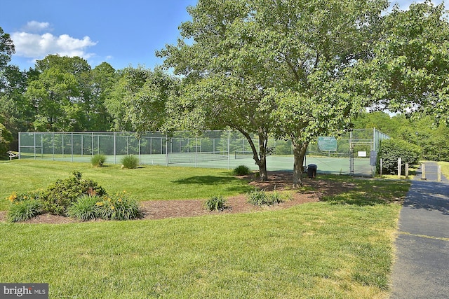 exterior space with a tennis court, fence, and a lawn