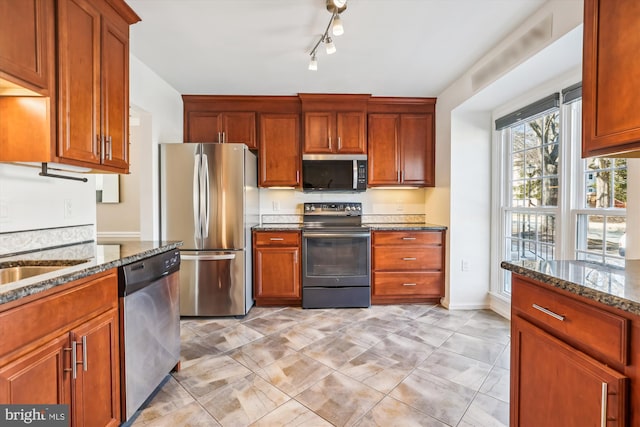 kitchen featuring dark stone counters, appliances with stainless steel finishes, brown cabinetry, and light tile patterned floors