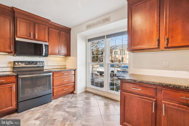 kitchen with dark stone countertops, appliances with stainless steel finishes, light tile patterned flooring, and baseboards