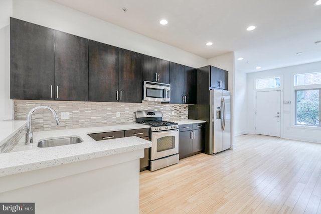 kitchen featuring sink, light hardwood / wood-style flooring, stainless steel appliances, light stone counters, and decorative backsplash