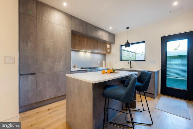 kitchen with sink, a kitchen breakfast bar, hanging light fixtures, a center island, and light wood-type flooring