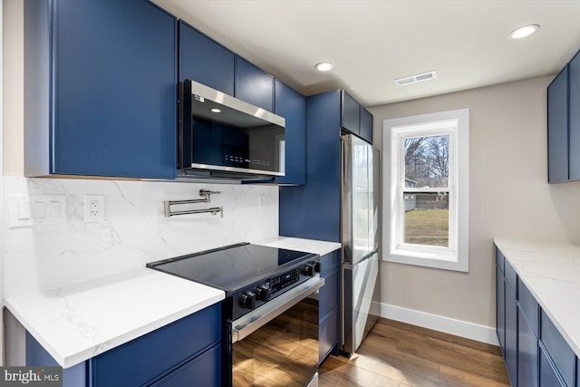 kitchen featuring decorative backsplash, blue cabinets, stainless steel appliances, and light stone countertops