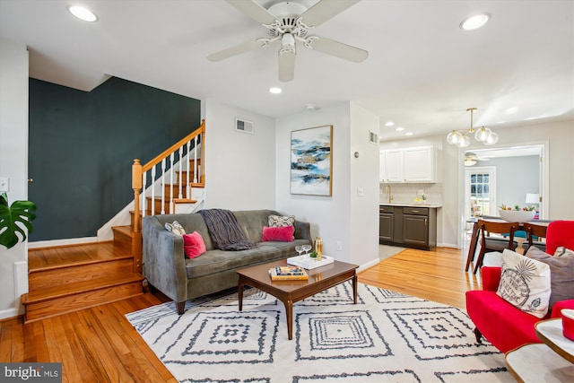 living room featuring ceiling fan with notable chandelier and light wood-type flooring