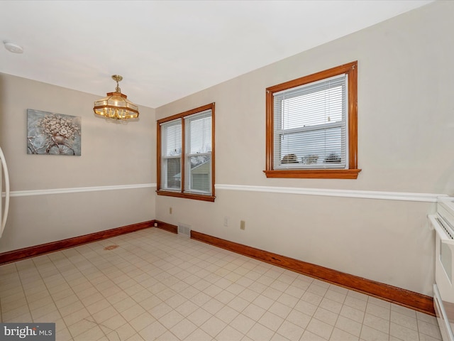 spare room featuring visible vents, an inviting chandelier, a wealth of natural light, and baseboards