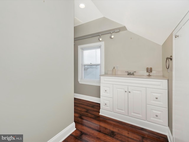 bathroom featuring baseboards, lofted ceiling, wood finished floors, rail lighting, and vanity