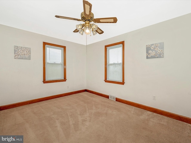 carpeted empty room featuring a ceiling fan, visible vents, and baseboards