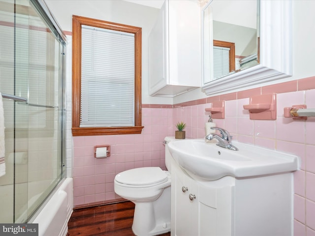 full bathroom with toilet, wood finished floors, combined bath / shower with glass door, vanity, and tile walls