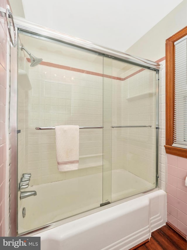 bathroom featuring wood finished floors, tile walls, and bath / shower combo with glass door