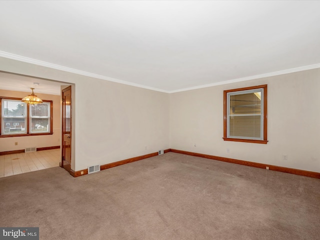 carpeted spare room featuring baseboards, visible vents, a chandelier, and ornamental molding