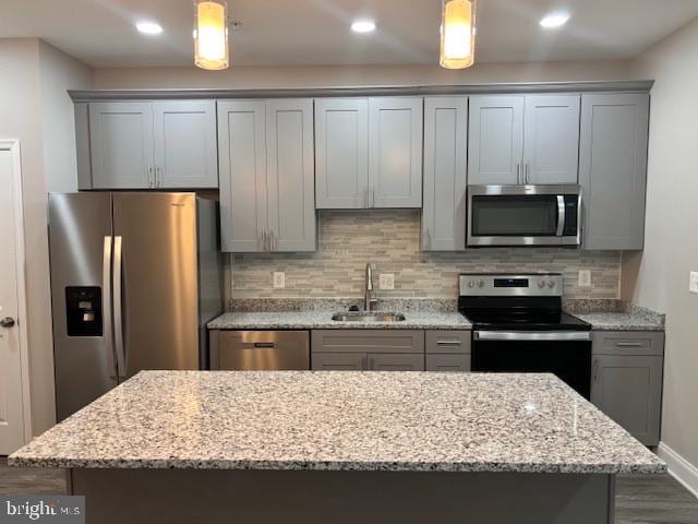 kitchen featuring light stone counters, sink, stainless steel appliances, and hanging light fixtures