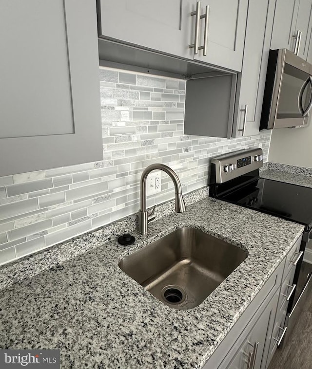 kitchen with appliances with stainless steel finishes, tasteful backsplash, sink, light stone counters, and dark wood-type flooring