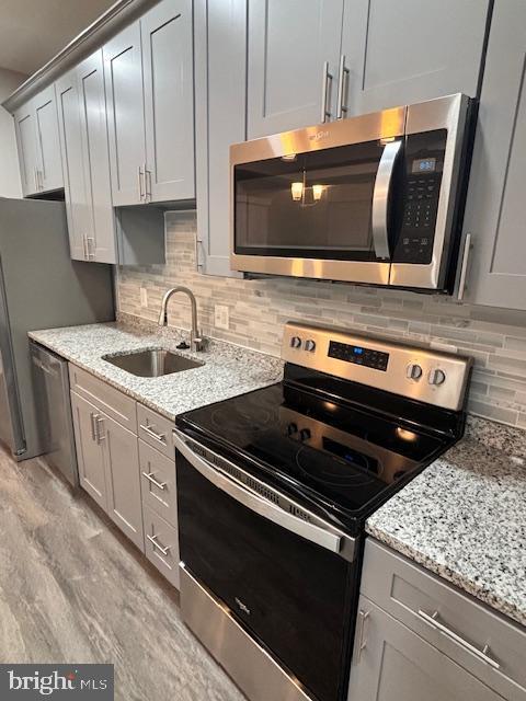 kitchen featuring stainless steel appliances, light stone countertops, sink, and decorative backsplash