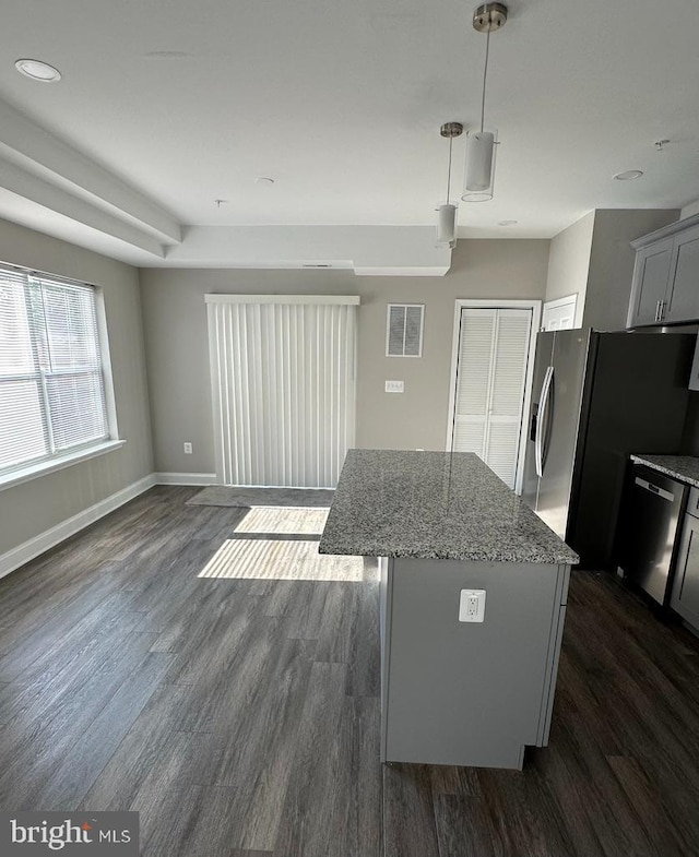 kitchen featuring stainless steel appliances, dark hardwood / wood-style floors, light stone countertops, a kitchen island, and decorative light fixtures