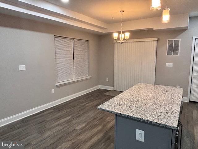 kitchen with dark hardwood / wood-style floors, light stone countertops, a kitchen island, decorative light fixtures, and a raised ceiling