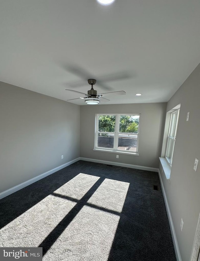 empty room with ceiling fan and dark colored carpet