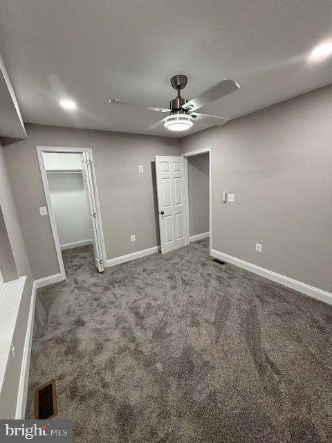 unfurnished bedroom featuring a walk in closet, ceiling fan, and carpet