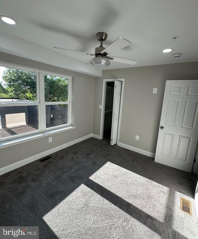 unfurnished bedroom with dark colored carpet, ceiling fan, and a closet