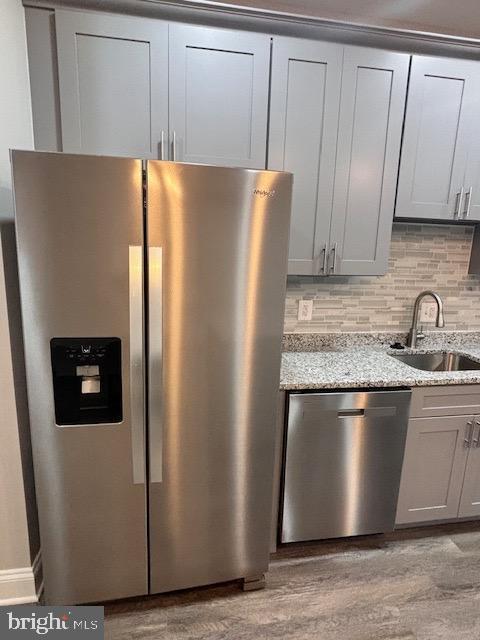 kitchen with light stone counters, sink, stainless steel appliances, and light wood-type flooring