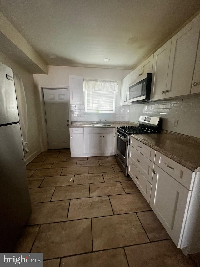 kitchen with tasteful backsplash, appliances with stainless steel finishes, sink, and white cabinets