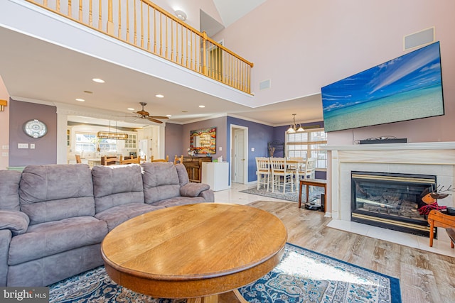 living room with crown molding, ceiling fan, a high ceiling, light hardwood / wood-style floors, and a tiled fireplace