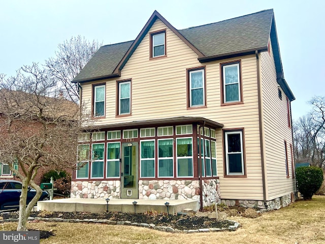 view of front of property featuring a shingled roof, a front yard, and stone siding