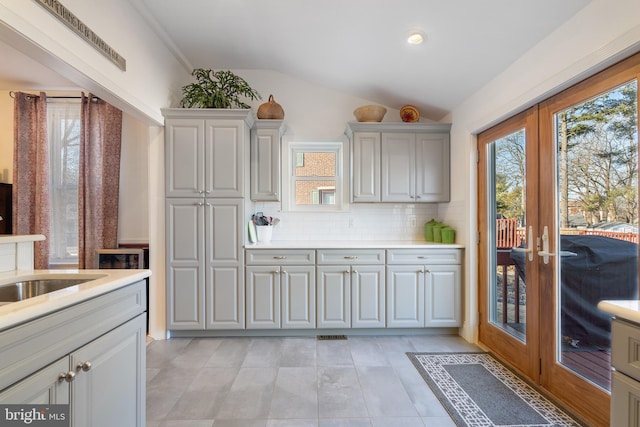 kitchen featuring french doors, lofted ceiling, gray cabinets, light countertops, and decorative backsplash