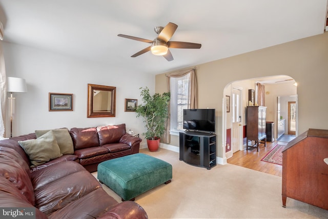 living area with a ceiling fan, arched walkways, light colored carpet, and baseboards