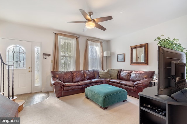 living area with stairway, a ceiling fan, and light colored carpet