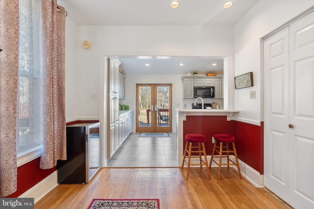 kitchen with french doors, light countertops, stainless steel microwave, light wood-style floors, and a kitchen bar