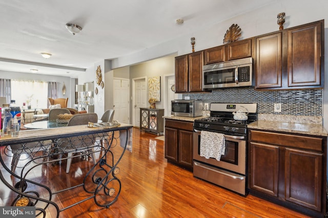 kitchen featuring appliances with stainless steel finishes, light stone counters, dark hardwood / wood-style flooring, dark brown cabinets, and tasteful backsplash