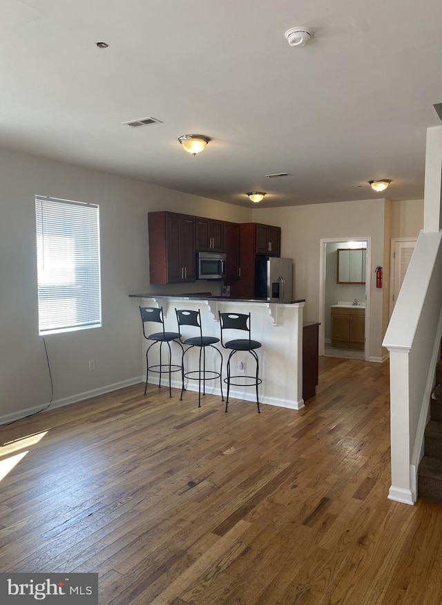 kitchen featuring a breakfast bar, dark wood-style flooring, visible vents, appliances with stainless steel finishes, and a peninsula