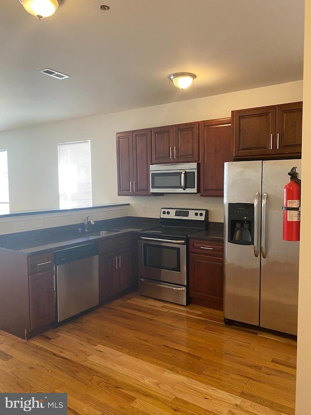 kitchen with dark countertops, visible vents, appliances with stainless steel finishes, a sink, and light wood-type flooring